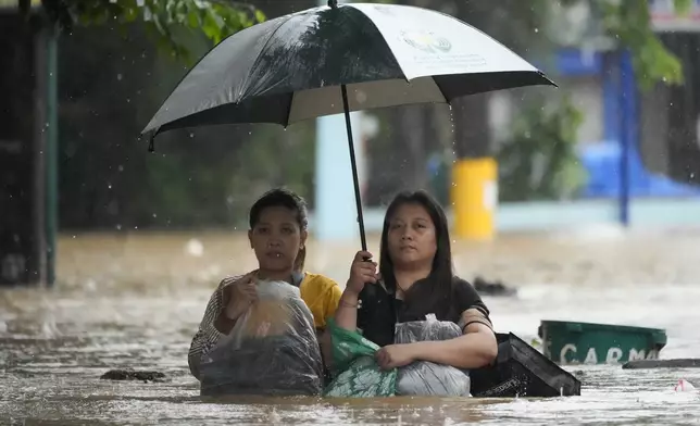 Residents protect their belongings as they negotiate a flooded street caused by heavy rains from Tropical Storm Yagi, locally called Enteng, in Cainta, Rizal province, Philippines, Monday, Sept. 2, 2024. (AP Photo/Aaron Favila)