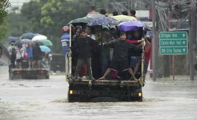 Commuters hold tight as they cross a flooded street caused by heavy rains from Tropical Storm Yagi, locally called Enteng, on Monday, Sept. 2, 2024, in Cainta, Rizal province, Philippines. (AP Photo/Aaron Favila)