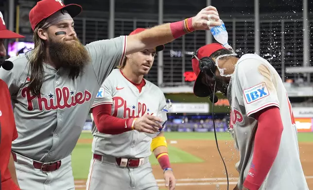 Philadelphia Phillies' Brandon Marsh, left, and Bryson Stott, center, douse Johan Rojas, right, as he is interviewed after a baseball game against the Miami Marlins, Friday, Sept. 6, 2024, in Miami. (AP Photo/Lynne Sladky)