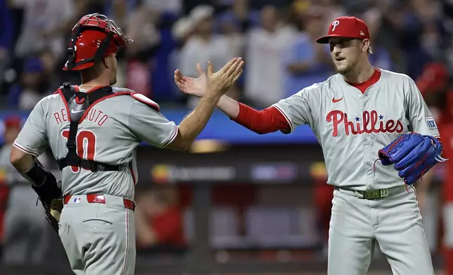 Philadelphia Phillies relief pitcher Jeff Hoffman, right, and catcher J.T. Realmuto (10) celebrate after defeating the New York Mets in a baseball game Friday, Sept. 20, 2024, in New York. (AP Photo/Adam Hunger)