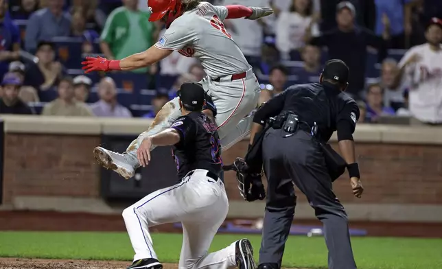 Philadelphia Phillies' Alec Bohm, top left, is tagged out by New York Mets starting pitcher David Peterson, bottom left, while trying to score on a fielder's choice during the third inning of a baseball game Friday, Sept. 20, 2024, in New York. Home plate umpire Edwin Moscoso, right, looks on. (AP Photo/Adam Hunger)