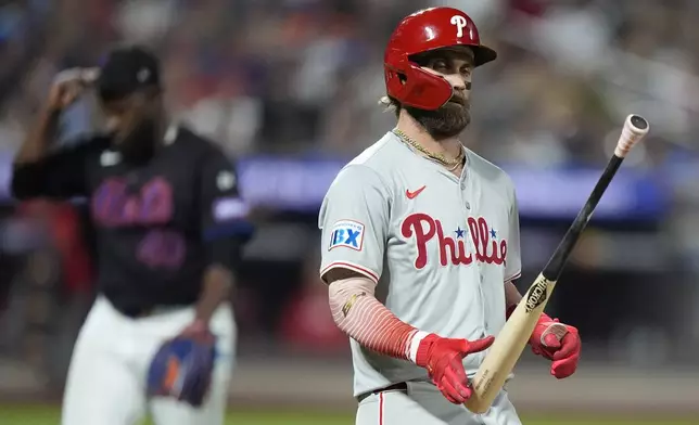 Philadelphia Phillies' Bryce Harper, right, passes New York Mets pitcher Luis Severino as he flips the bat to himself after grounding out during the fifth inning of a baseball game, Thursday, Sept. 19, 2024, in New York. (AP Photo/Frank Franklin II)