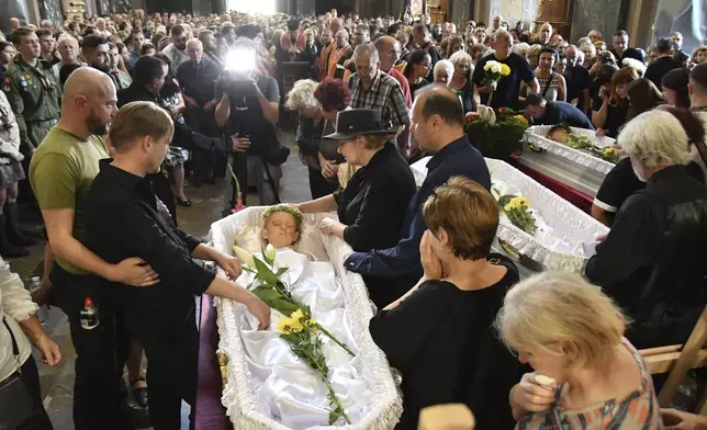 People mourn near the coffins of Yaroslav Bazylevych's, second left, family members during their funeral service in the Garrison Church in Lviv, Ukraine, Friday, Sept. 6, 2024. (AP Photo/Mykola Tys)