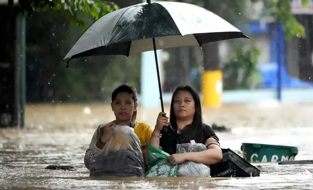 Residents protect their belongings as they negotiate a flooded street caused by heavy rains from Tropical Storm Yagi, locally called Enteng, in Cainta, Rizal province, Philippines, Monday, Sept. 2, 2024. (AP Photo/Aaron Favila)