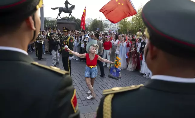 An elderly woman dances while the Military Band of the Chinese People's Liberation Army performs at the Historical Museum prior to the closing of Spasskaya Tower International Military Music Festival in Red Square, with the statue of Soviet Marshal Georgy Zhukov in the background, in Moscow, Russia, Sunday, Sept. 1, 2024, with foreign participants include Belarus, Venezuela, Egypt, China, Thailand, Turkey, South Africa and Guinea. (AP Photo/Alexander Zemlianichenko)