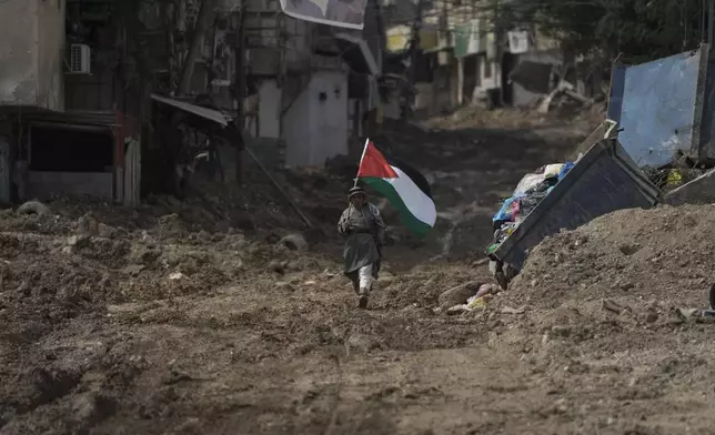 Palestinian activist Khairi Hanoon walks with the Palestinian flag on a damaged road following an Israeli army raid in Tulkarem, West Bank, on Tuesday, Sept. 3, 2024. (AP Photo/Majdi Mohammed)