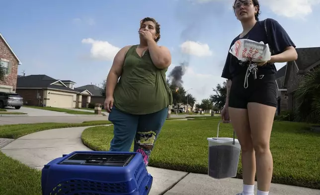 Meadow Way Drive residents Maddy Graham, right, and Ashley Cordova are self evacuating with cat, Mitzi, as the pipeline fire burns in the background Monday, Sept. 16, 2024, in Deer Park, Texas. (Yi-Chin Lee/Houston Chronicle via AP)