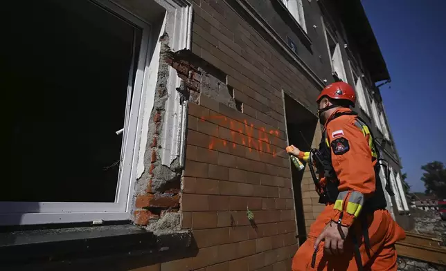 On this handout photo provided by the State Fire Service of Poland, a firefighter writes "Zakaz" (Entry prohibited), on a building damaged by following heavy flooding in the town of Stronie Slaskie, southwestern Poland, Wednesday, Sept. 18, 2024. (Tomasz Fijołek/KG PSP via AP)