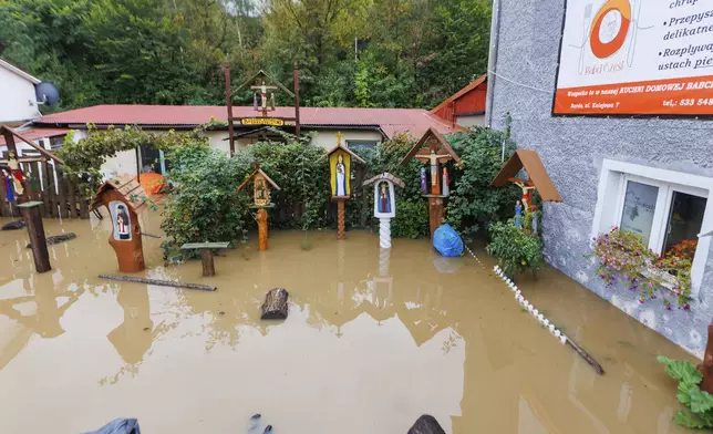 A flooded backyard with carved wood religious figures in Kłodzko, southwest Poland, as days of unusually heavy rain have swollen rivers and spilled over embankments in the region, on Sunday, Sept. 15, 2024. (AP Photo/Krzysztof Zatycki)