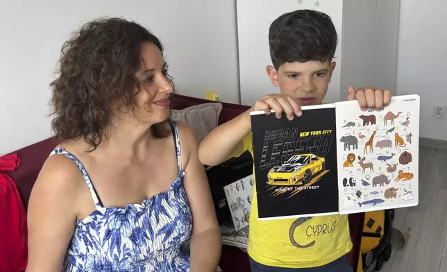 Sava Trypolsky, a 7-year-old boy from Ukraine, holds up school supplies with his mother Oksana Trypolska, in Jablonna, Poland on Friday, Aug. 30, 2024. (AP Photo/Vanessa Gera)