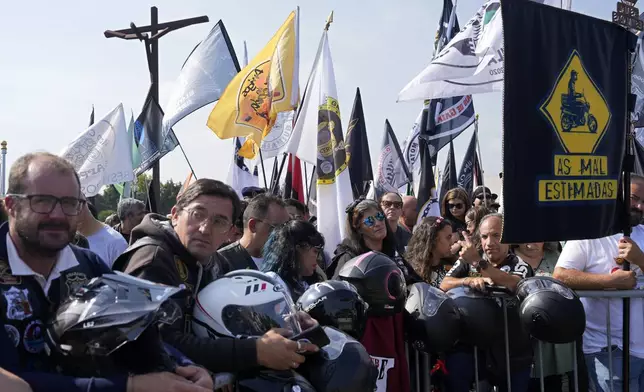 Motorcyclists holding their helmets and their groups' banners gather at the Roman Catholic holy shrine of Fatima to attend the IX Pilgrimage of the Blessing of Helmets that draws tens of thousands, in Fatima, Portugal, Sunday, Sept. 22, 2024. (AP Photo/Ana Brigida)