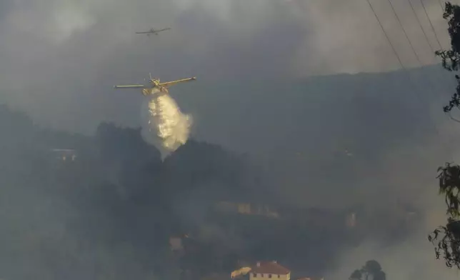 Firefighting airplanes drop water on a fire burning near houses in Sever do Vouga, a town in northern Portugal that has been surrounded by wildfires, Monday, Sept. 16, 2024. (AP Photo/Bruno Fonseca)