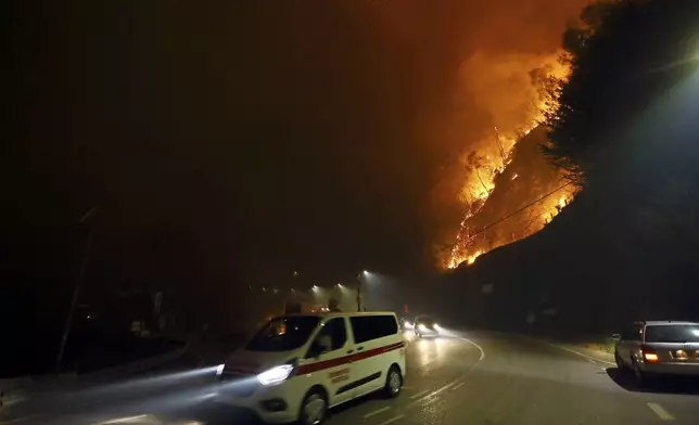 Vehicles drive past a fire burning by the road near Sever do Vouga, a town in northern Portugal that has been surrounded by forest fires, Monday night, Sept. 16, 2024. (AP Photo/Bruno Fonseca)