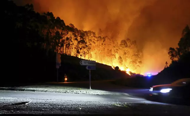 A car drives past a road closed by police as a wildfire burns close to it, near Sever do Vouga, a town in northern Portugal that has been surrounded by forest fires, Monday night, Sept. 16, 2024. (AP Photo/Bruno Fonseca)