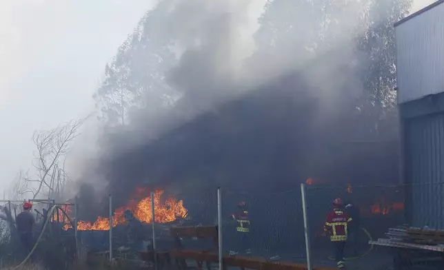 Firefighters work to control a fire next to a metalworking warehouse in Sever do Vouga, a town in northern Portugal that has been surrounded by forest fires, Monday, Sept. 16, 2024. (AP Photo/Bruno Fonseca)