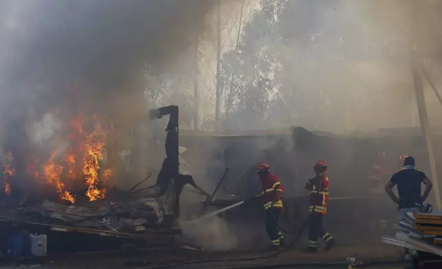 Firefighters work to control a fire next to warehouses in Sever do Vouga, a town in northern Portugal that has been surrounded by wildfires fires, Monday, Sept. 16, 2024. (AP Photo/Bruno Fonseca)