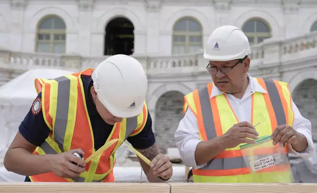 Tyler Smith, a woodcrafter with the Architect of the Capitol, and Herbert Melgar, a painter, measure out the nail placement for Congress members to hammer for the First Nail Ceremony marking the beginning of construction of the 2025 Presidential Inauguration platform at the Capitol, Wednesday, Sept. 18, 2024, in Washington. (AP Photo/Mariam Zuhaib)