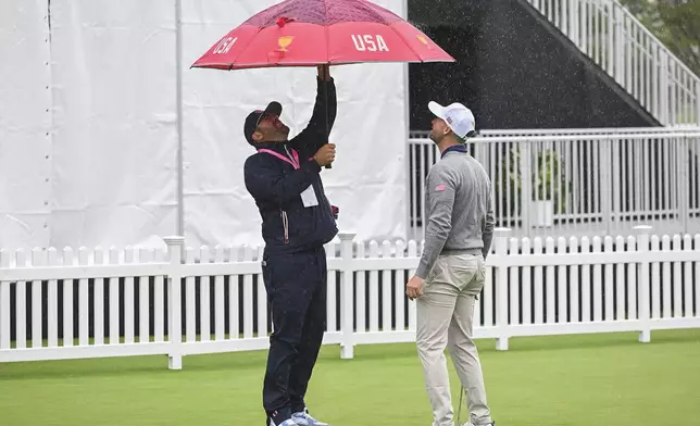 United States team member Wyndham Clark, right, looks on as his caddy adjusts an umbrella during practice at the Presidents Cup at the Royal Montreal Golf Club on Monday, Sept. 23, 2024, in Montreal. (Graham Hughes/The Canadian Press via AP)