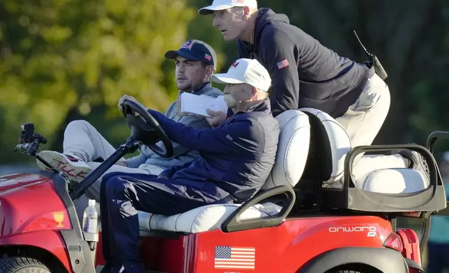 United States team captain Jim Furyk, top, grabs a ride with United States team member Keegan Bradley, left, and Mike "Fluff" Cowan driving during their fourth-round foursomes match at the Presidents Cup golf tournament at Royal Montreal Golf Club, Saturday, Sept. 28, 2024, in Montreal. (Frank Gunn/The Canadian Press via AP)