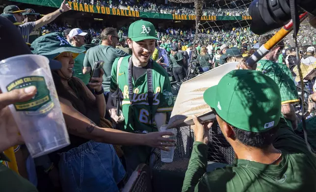 Grounds crew member Kyle Yamashita, front right, pours dirt from the field into containers for fans from a shovel after the Oakland Athletics defeated the Texas Rangers in a baseball game at the Coliseum in Oakland, Calif., Thursday, Sept. 26, 2024. It was the Athletics final home game at the Coliseum. (Carlos Avila Gonzalez/San Francisco Chronicle via AP)