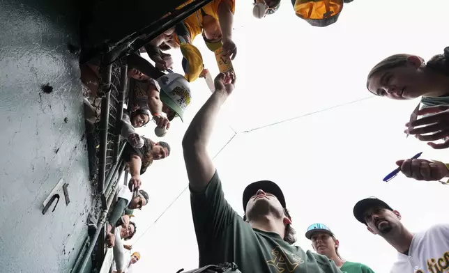 Oakland Athletics' Jacob Wilson, center, sign autographs for fans before a baseball game against the Texas Rangers, Thursday, Sept. 26, 2024, in Oakland, Calif. (AP Photo/Godofredo A. Vásquez)