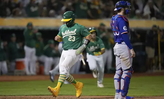 Oakland Athletics' Shea Langeliers (23) scores next to Texas Rangers catcher Jonah Heim on Zack Gelof's sacrifice fly during the sixth inning of a baseball game Tuesday, Sept. 24, 2024, in Oakland, Calif. (AP Photo/Godofredo A. Vásquez)