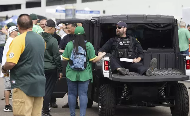 A police officer interacts with fans outside the Oakland Coliseum before a baseball game between the Oakland Athletics and the Texas Rangers Thursday, Sept. 26, 2024, in Oakland, Calif. (AP Photo/Benjamin Fanjoy)