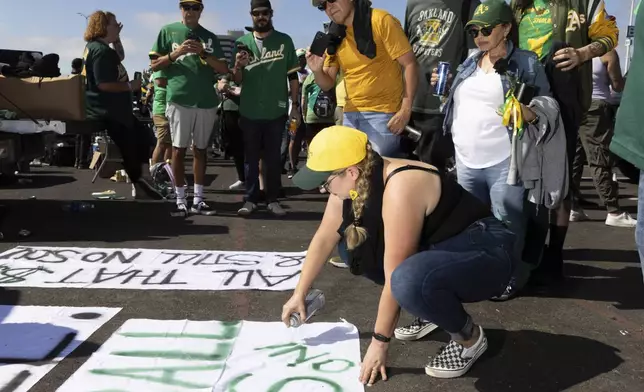 Michelle Leon paints a sign outside the Oakland Coliseum before a baseball game between the Oakland Athletics and the Texas Rangers Thursday, Sept. 26, 2024, in Oakland, Calif. (AP Photo/Benjamin Fanjoy)