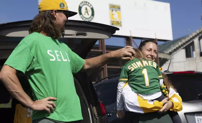 Jacob Sutter, left, stands as Marta Sutter holds their daughter, 3-year-old Summer Sutter outside the Oakland Coliseum before a baseball game between the Oakland Athletics and the Texas Rangers Thursday, Sept. 26, 2024, in Oakland, Calif. (AP Photo/Benjamin Fanjoy)