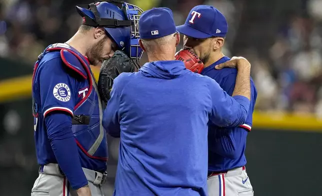 Texas Rangers pitching coach Mike Maddux, middle, talks with his catcher Jonah Heim, left, and pitcher Nathan Eovaldi, right, during the fourth inning of a baseball game against the Arizona Diamondbacks, Tuesday, Sept. 10, 2024, in Phoenix. (AP Photo/Darryl Webb)