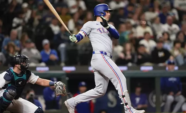 Texas Rangers' Nathaniel Lowe follows through on an RBI single to score Wyatt Langford as Seattle Mariners catcher Cal Raleigh looks on during the eighth inning of a baseball game Thursday, Sept. 12, 2024, in Seattle. (AP Photo/Lindsey Wasson)