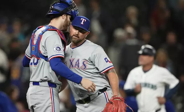 Texas Rangers catcher Jonah Heim, left, greets relief pitcher Kirby Yates, right, after Yates earned the save in a 5-4 win over the Seattle Mariners in a baseball game Thursday, Sept. 12, 2024, in Seattle. (AP Photo/Lindsey Wasson)