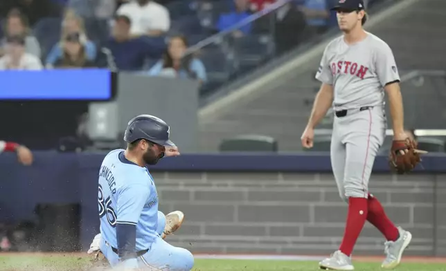 Toronto Blue Jays' Davis Schneider, left, scores a run as Boston Red Sox pitcher Lucas Sims, right, looks on during the fifth inning of a baseball game in Toronto, Tuesday, Sept. 24, 2024. (Chris Young/The Canadian Press via AP)