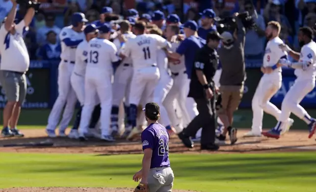 Members of Los Angeles Dodgers celebrate after Mookie Betts hit a walk-off solo home run as Colorado Rockies third baseman Ryan McMahon, below, walks off the field during the ninth inning of a baseball game, Sunday, Sept. 22, 2024, in Los Angeles. The Dodgers won 6-5. (AP Photo/Mark J. Terrill)