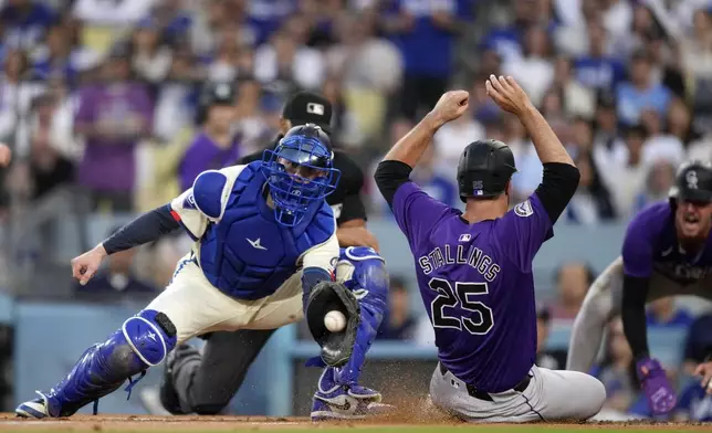 Colorado Rockies' Jacob Stallings, center, scores on as double by Ezequiel Tovar as Los Angeles Dodgers catcher Hunter Feduccia puts a late take on him during the second inning of a baseball game, Saturday, Sept. 21, 2024, in Los Angeles. (AP Photo/Mark J. Terrill)