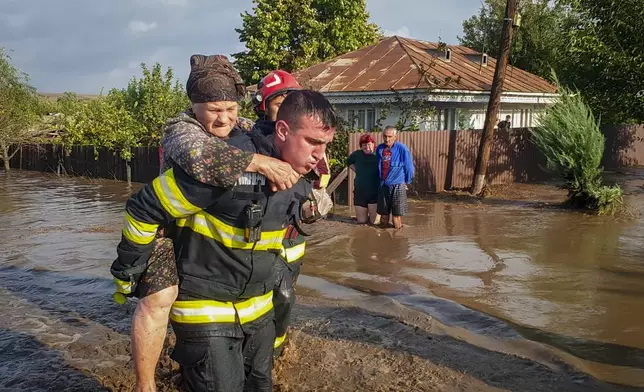 In this photo released by the Romanian Emergency Services Galati (ISU Galati), a rescuer carries a woman in Pechea, Romania, Saturday, Sept. 14, 2024 after torrential rainstorms left scores of people stranded in flooded areas. (Romanian Emergency Services - ISU Galati via AP)