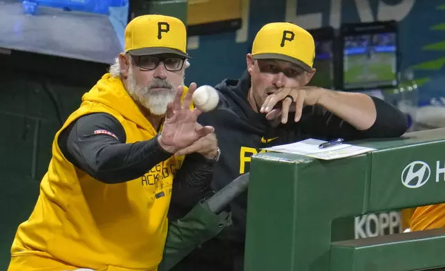 Pittsburgh Pirates manager Derek Shelton, left, takes a toss from Isiah Kiner-Falefa in the on-deck circle while standing in the dugout with bench coach Don Kelly, right, during the ninth inning of a baseball game against the Kansas City Royals in Pittsburgh, Friday, Sept. 13, 2024. Shelton tossed the ball to a nearby fan. (AP Photo/Gene J. Puskar)