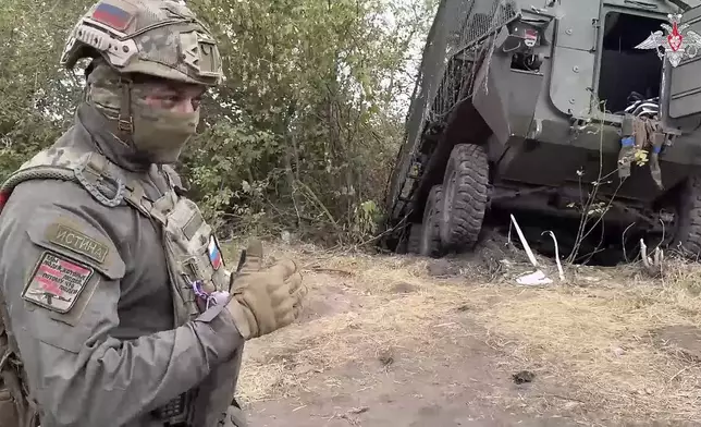 In this photo taken from video released by the Russian Defense Ministry on Friday, Sept. 13, 2024, a Russian soldier stands next to a damaged Ukrainian military vehicle in the Russian - Ukrainian border area in the Kursk region, Russia. (Russian Defense Ministry Press Service photo via AP)