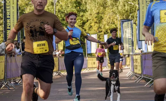 A woman runs with her dog during a charity run to raise awareness on Ukrainian prisoners of war held by Russia, in Kyiv, Ukraine, Saturday, Sept. 14, 2024. (AP Photo/Evgeniy Maloletka)