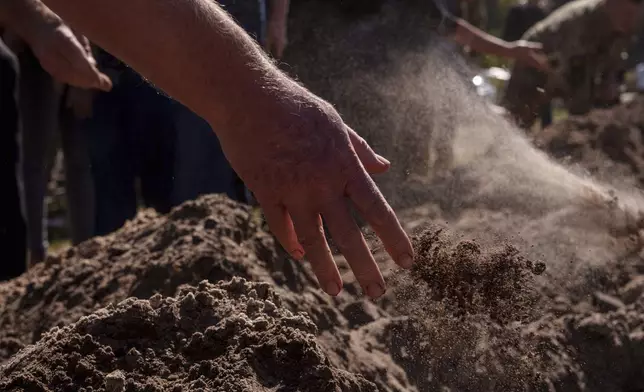 People throw three handfuls of soil into a grave during the funeral ceremony of six Ukrainian servicemen killed in a Russian rocket attack at a Ukrainian military academy, during their funeral ceremony in Poltava, Ukraine, Saturday Sept. 7, 2024. (AP Photo/Evgeniy Maloletka)