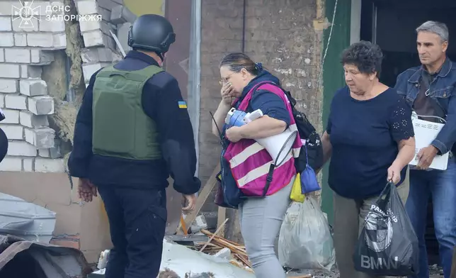 In this photo provided by the Ukrainian Emergency Service, residents carrying belongings leave their ruined home after Russia attacked the city with guided bombs overnight in Zaporizhzhia, Ukraine, Sunday, Sept. 29, 2024. (Ukrainian Emergency Service via AP)