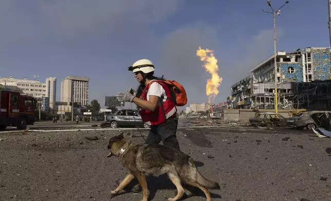 A rescue dog handler walks in front of a business center damaged by a Russian attack in Kharkiv, Ukraine, Sunday, Sept. 1 2024. (AP Photo/Yevhen Titov)