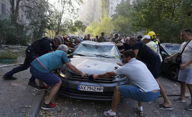 Emergency services and local residents move a damaged car after a Russian aerial bomb struck a multi-story residential building in Kharkiv, Ukraine, Sunday Sept. 15, 2024. (AP Photo/Andrii Marienko)