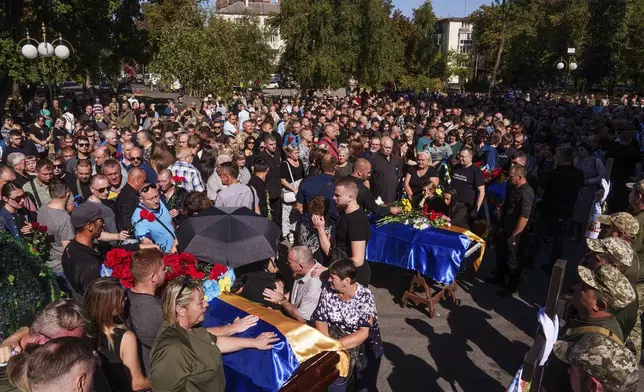 Relatives and friends mourn near the coffins of six Ukrainian servicemen killed in a Russian rocket attack at a Ukrainian military academy, during their funeral ceremony in Poltava, Ukraine, Saturday Sept. 7, 2024. (AP Photo/Evgeniy Maloletka)