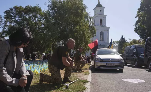 Ukrainian servicemen kneel during the funeral ceremony of six of their comrades who were killed in a Russian rocket attack at a Ukrainian military academy, in Poltava, Ukraine, Saturday Sept. 7, 2024. (AP Photo/Evgeniy Maloletka)