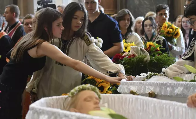 People mourn near the coffins of Yaroslav Bazylevych's family during the funeral service in the Garrison Church in Lviv, Ukraine, Friday, Sept. 6, 2024. Bazylevych's wife Yevgenia and their three daughters - Darina, 18, Emilia, 7, and Yaryna, 21 - were killed in Wednesday's Russian missile attack. (AP Photo/Mykola Tys)