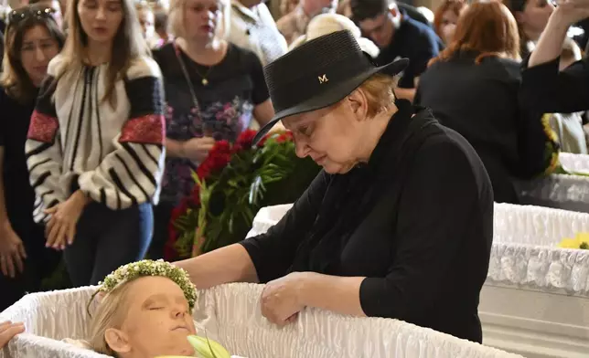 A relative mourns at the coffins of Yaroslav Bazylevych's family members during their funeral service in the Garrison Church in Lviv, Ukraine, Friday, Sept. 6, 2024. Bazylevych's wife Yevgenia and their three daughters - Darina, 18, Emilia, 7, and Yaryna, 21 - were killed in Wednesday's Russian missile attack. (AP Photo/Mykola Tys)