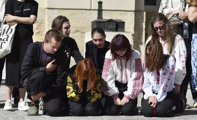 People kneel in respect during the funeral ceremony of Yaroslav Bazylevych's family members in Lviv, Ukraine, Friday, Sept. 6, 2024. Bazylevych's wife Yevgenia and their three daughters - Darina, 18, Emilia, 7, and Yaryna, 21 - were killed in Wednesday's Russian missile attack. (AP Photo/Mykola Tys)