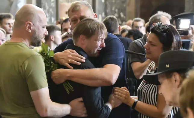 Friends hug Yaroslav Bazylevych during the funeral service for his family in the Garrison Church in Lviv, Ukraine, Friday, Sept. 6, 2024. Bazylevych's wife Yevgenia and their three daughters - Darina, 18, Emilia, 7, and Yaryna, 21 - were killed in Wednesday's Russian missile attack. (AP Photo/Mykola Tys)