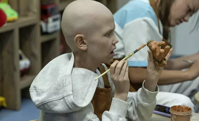 Kira Vertetska, 8, who is undergoing treatment in the oncology department at Okhmatdyt children's hospital in Kyiv, Ukraine, paints a clay figure, Thursday Sept. 19, 2024. (AP Photo/Anton Shtuka)